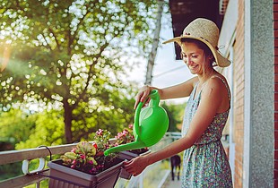 Frau wässert Blumen auf dem Balkon.